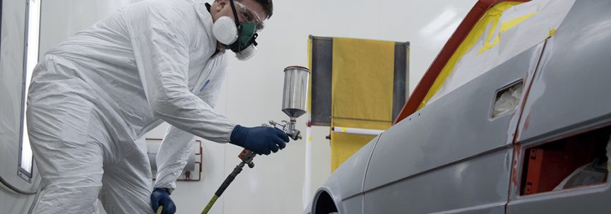 A photo of a student using an air sprayer on a sporty looking car